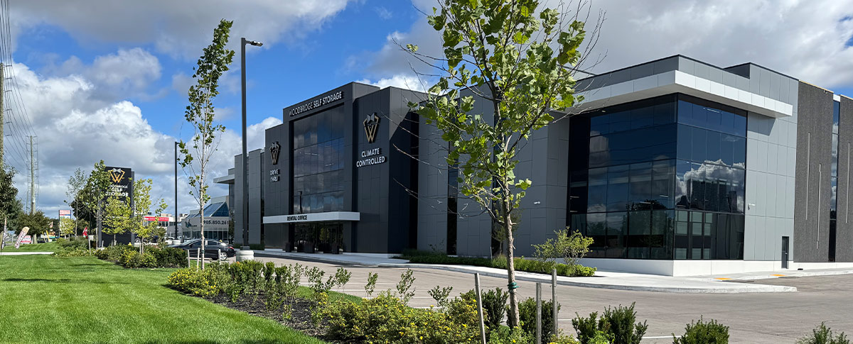 Modern exterior of Woodbridge Self Storage featuring a gray and black facade, large glass windows, a green lawn, and young trees. Signage reads "Climate Controlled" and "Rental Office."