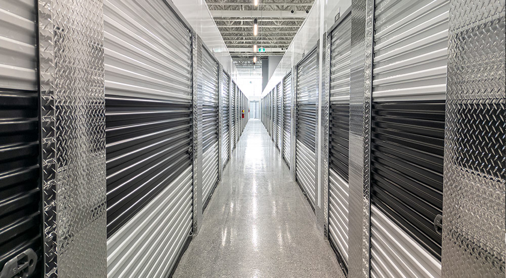 A long, brightly lit interior corridor lined with white and black storage units featuring shiny diamond-plate metal trim and a polished, reflective floor.