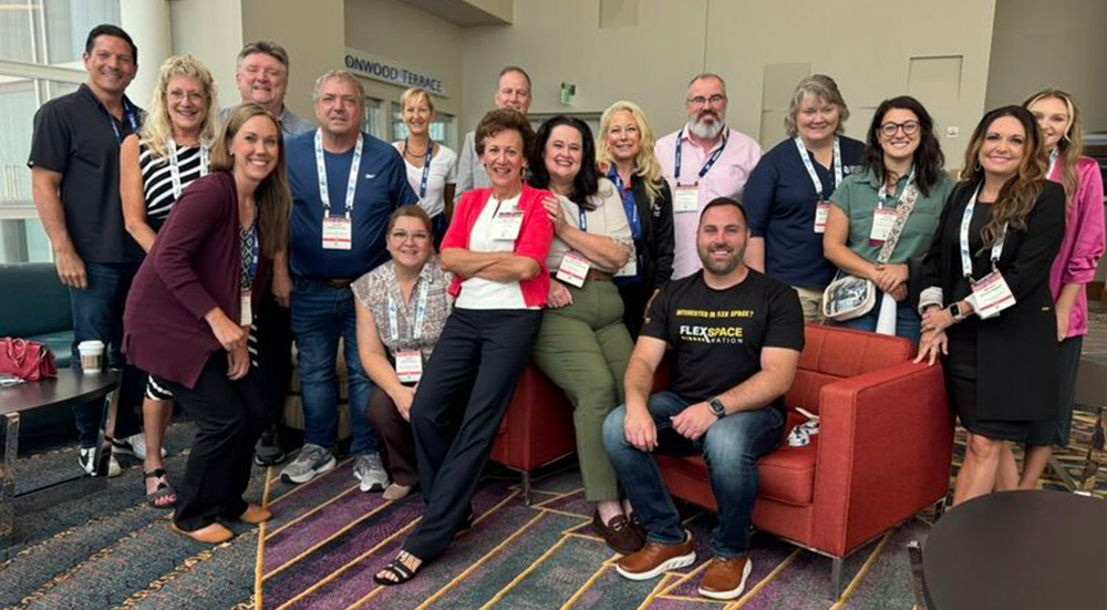 A large group photo of the Self-Storage Prayer Group standing and sitting together indoors. They are smiling at a conference or event, with many members wearing name badges on lanyards.