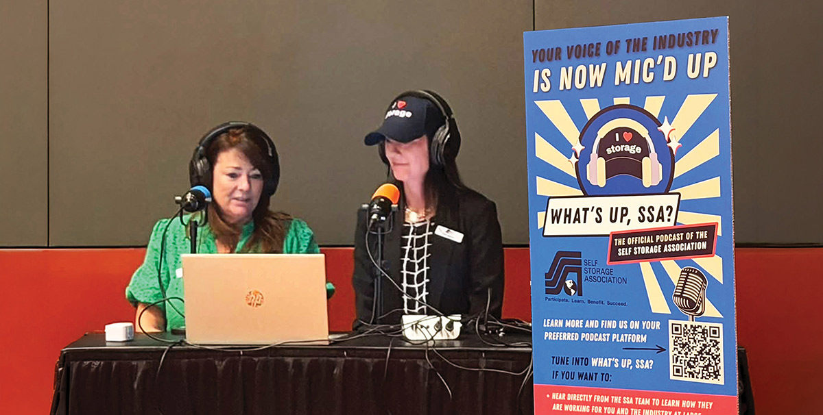 Two women recording the live What's Up, SSA? podcast's first episode at a horizontal orientated table against a wall