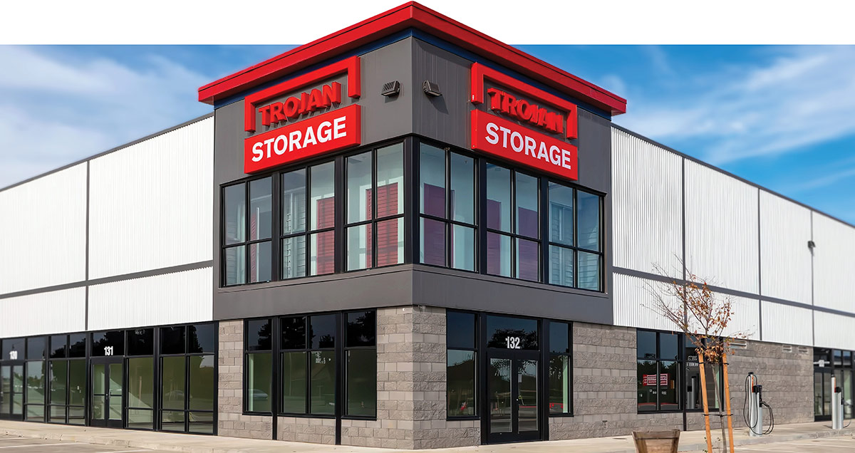 Exterior corner view of a Trojan Storage commercial facility featuring large windows and red signs.