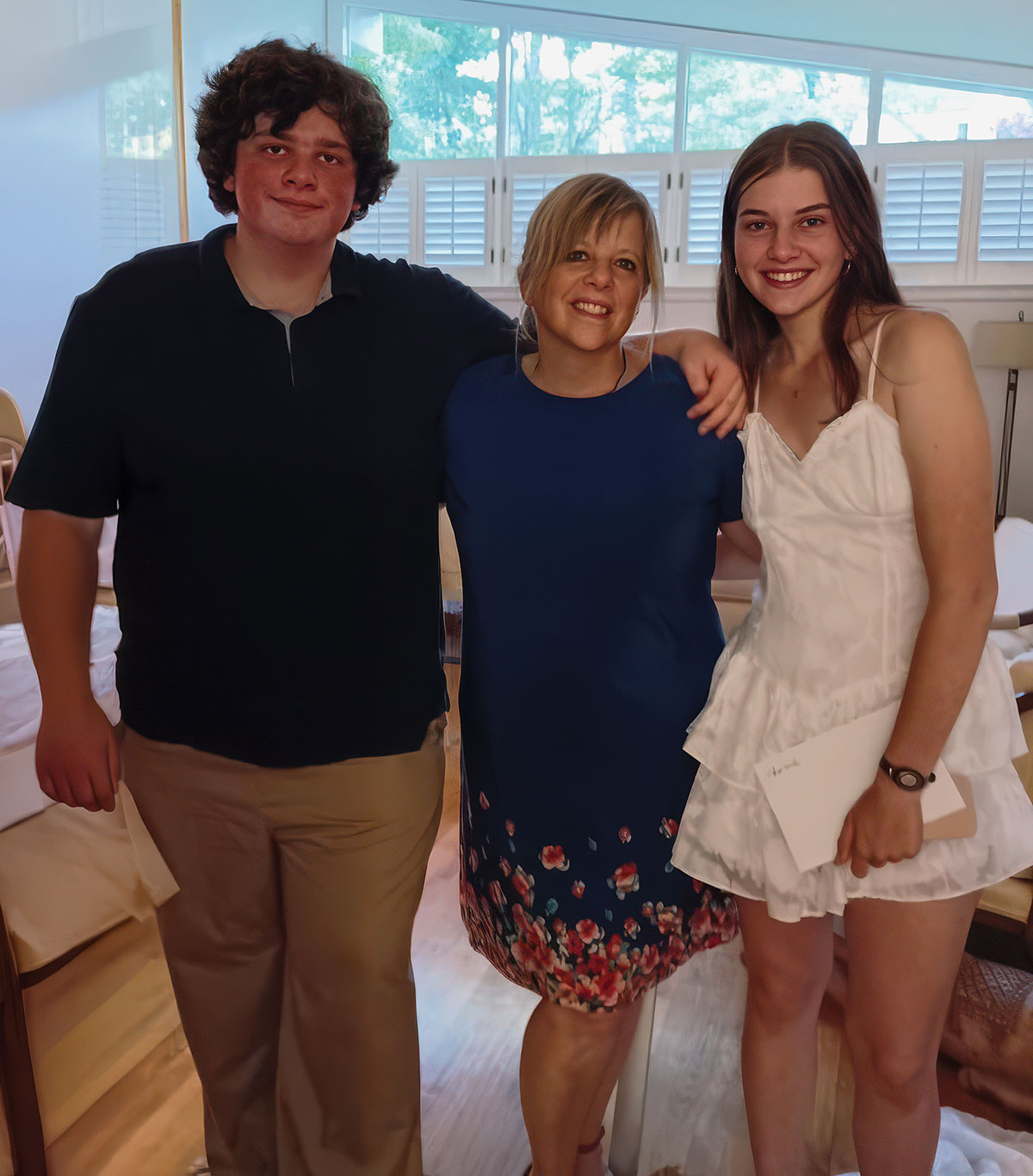 Kim Hoelting and her children posing together inside a brightly lit room of a house; White window shutters are visible in the background