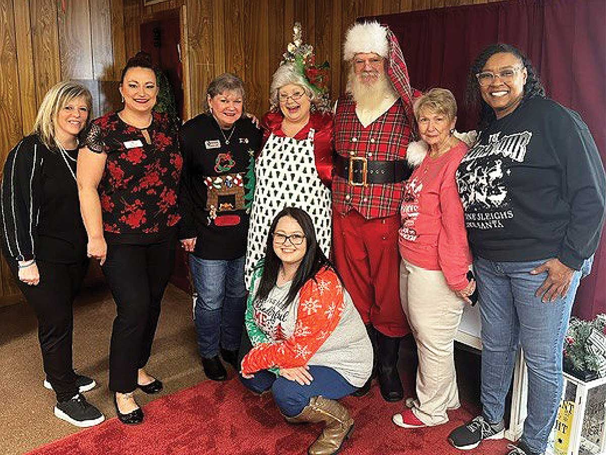Kim Hoelting and a group of people dressed in casual holiday attire who happen to be team members pose together with a man dressed as Santa Claus