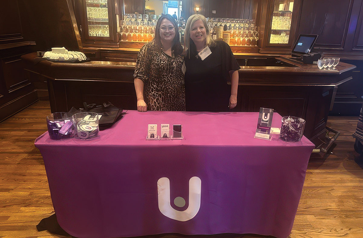 Kim Hoelting and another woman smiling together behind a promotional Universal Storage Group (USG) display table at an event
