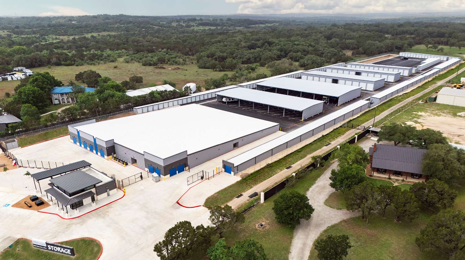 Aerial view of a large, modern self-storage facility featuring multiple long buildings, covered parking canopies, and a gated entrance.