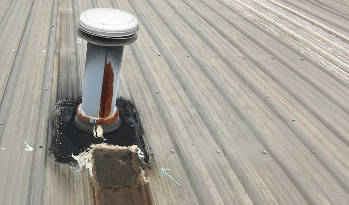 A metal roof vent pipe surrounded by thick, messy black and white sealant at its base. Dark brown rust stains run down the pipe and onto the corrugated metal roof panel.