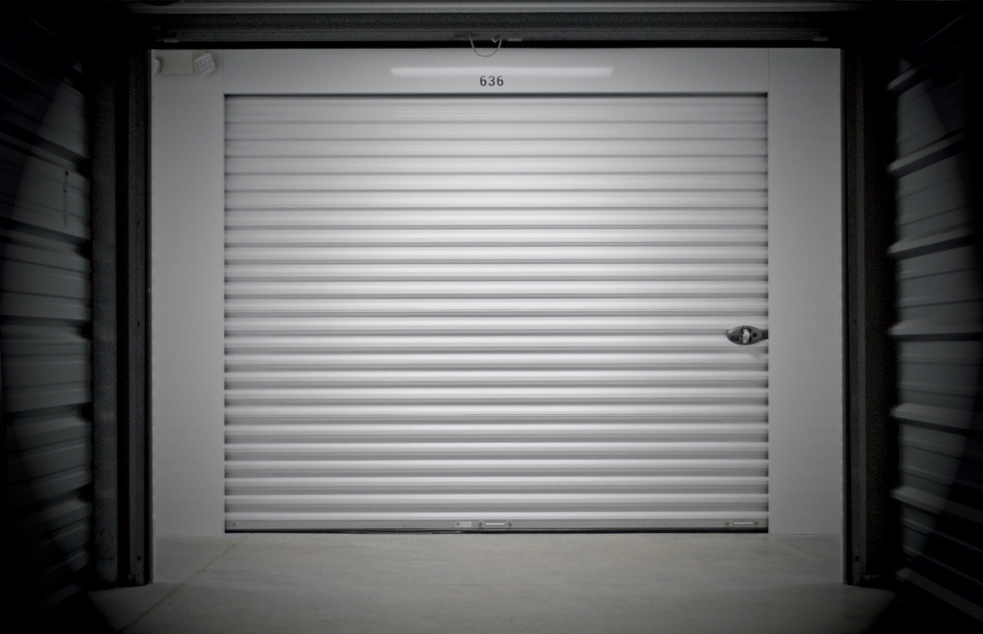 A bright white Trac-Rite roll-up self-storage unit door with the unit number 636 centered above it, viewed from inside a dimly lit hallway.