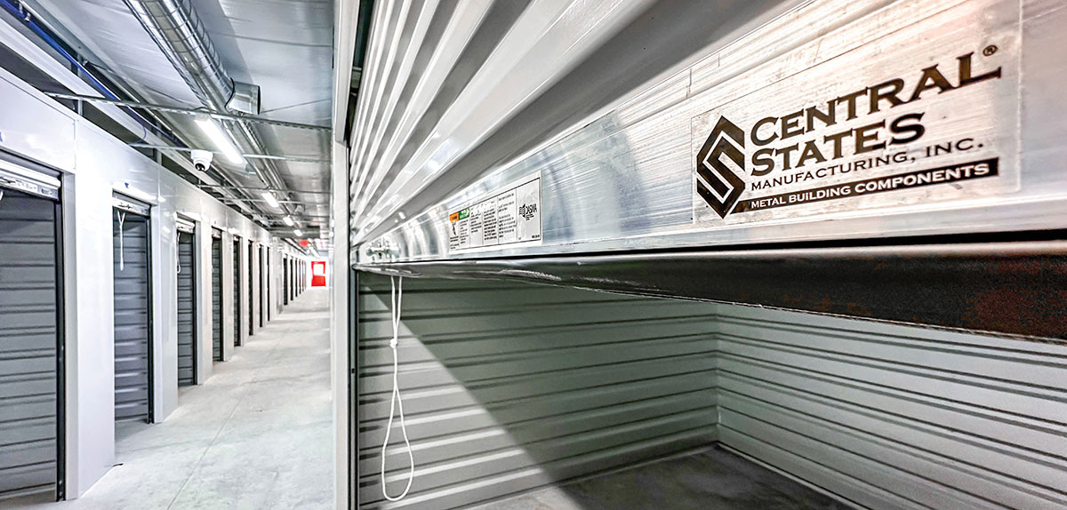 An indoor self-storage hallway featuring rows of metal storage units with roll-up doors.