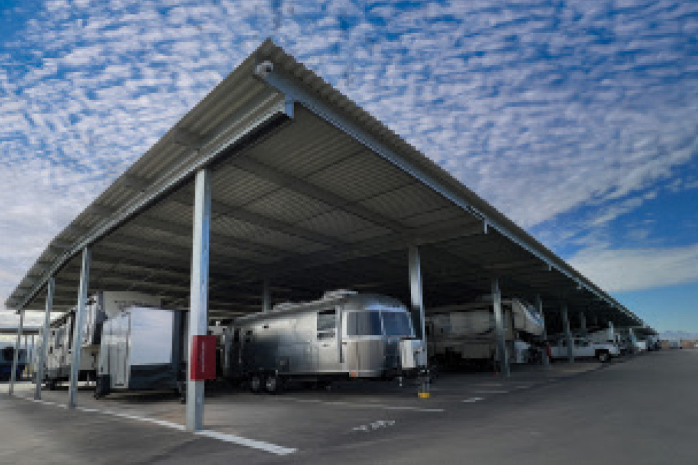 A silver Airstream trailer and other RVs parked under a large steel canopy structure at an outdoor storage facility.
