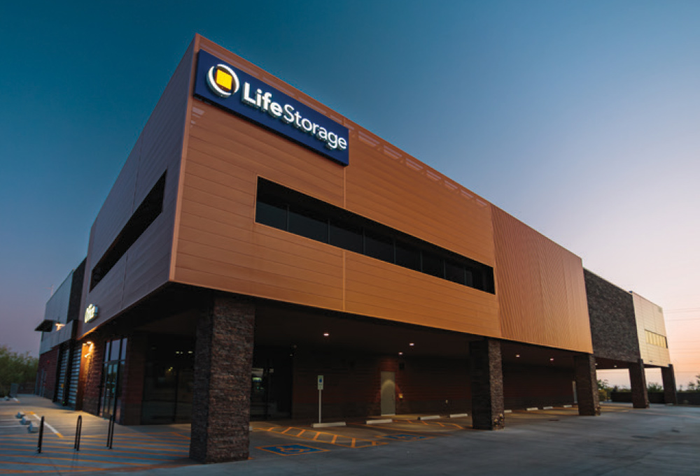 A modern Life Storage facility with a copper-colored facade and stone column supports under a clear twilight sky.