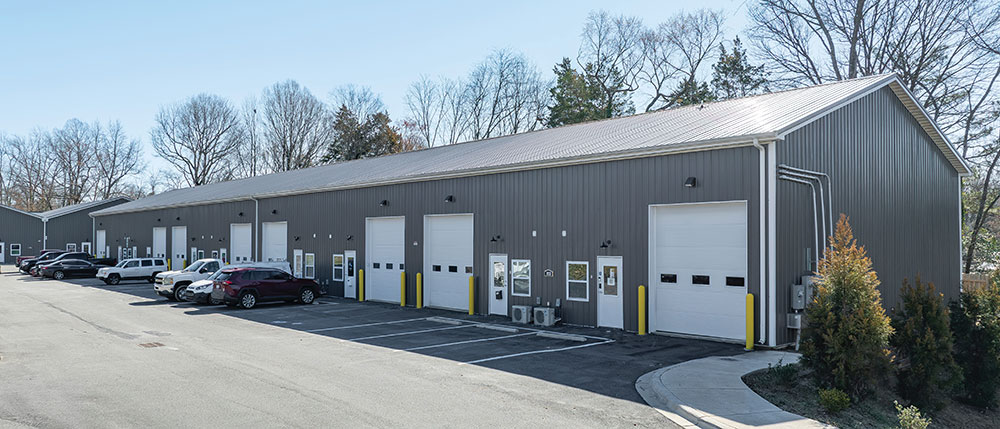 Wide exterior view of a long gray industrial building with several garage doors.
