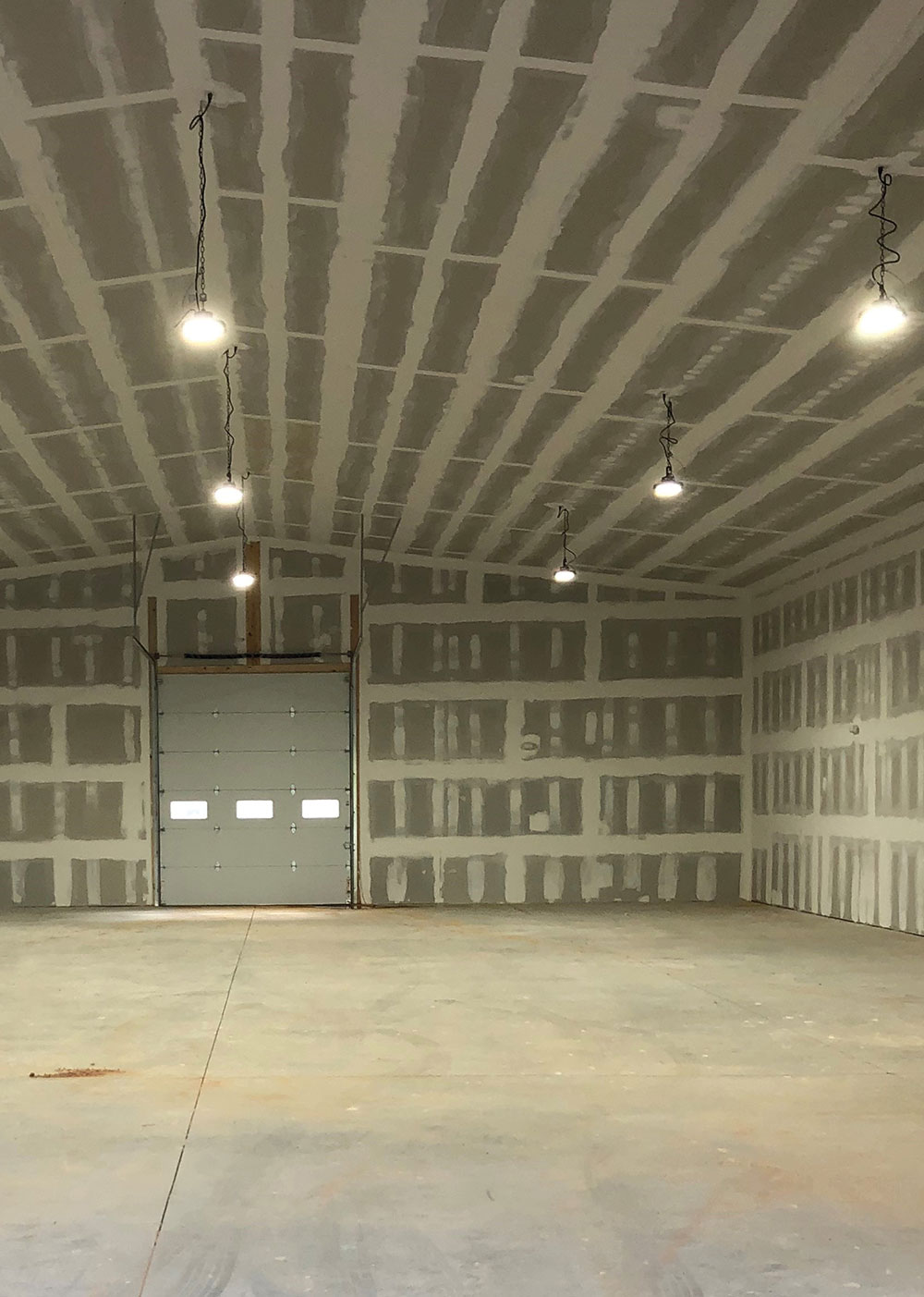 Large empty interior warehouse room with drywall and overhead light fixtures.