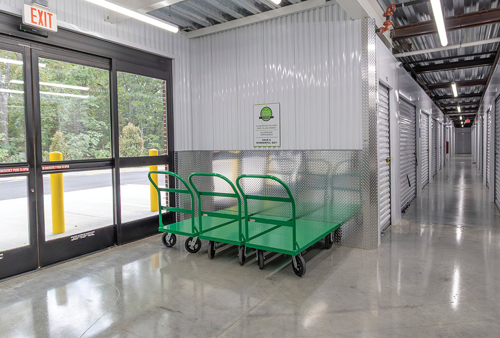 Three green flatbed moving carts inside a clean storage unit hallway.