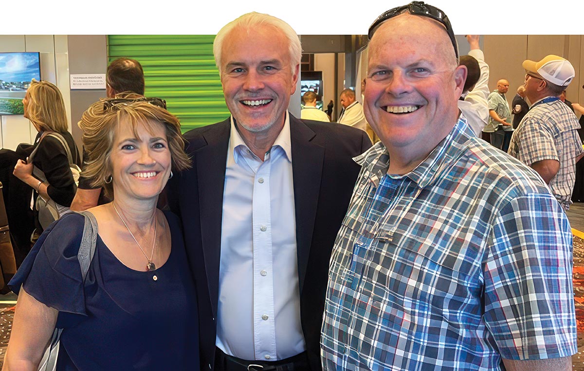 Mike Schofield smiling with two people at a trade show.