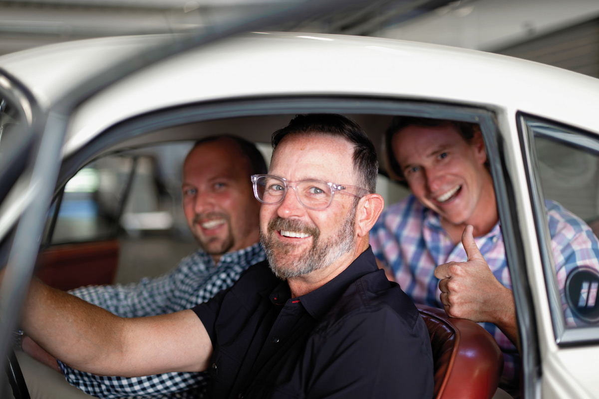 Dave King, David Brown, and Dave French smiling inside a vintage car.