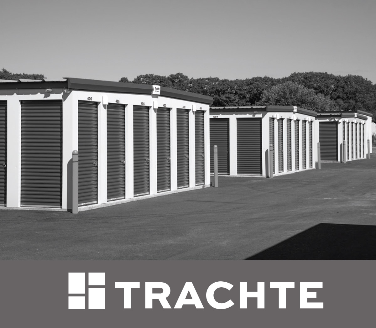 A black and white photo of outdoor self-storage units with roll-up doors and asphalt driveways. A dark gray banner at the bottom features the "TRACHTE" logo and brand name.
