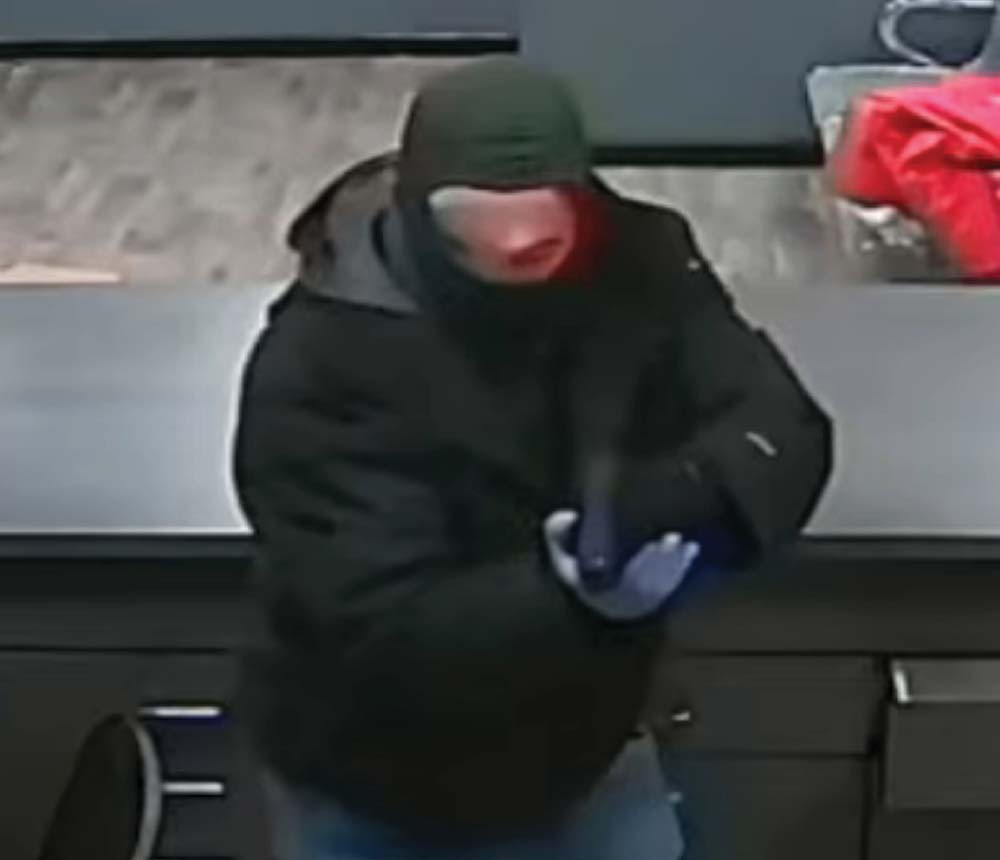 Low-resolution surveillance image of a suspect wearing a dark coat and face mask.