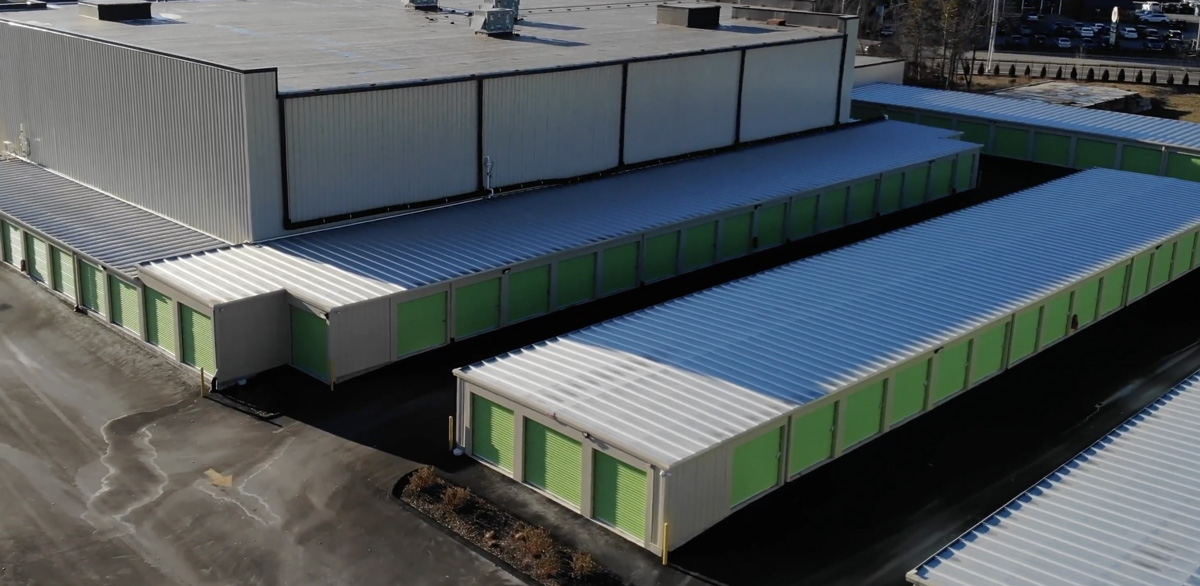 High-angle aerial view of a self-storage complex with long single-story rows of green garage-door storage units.