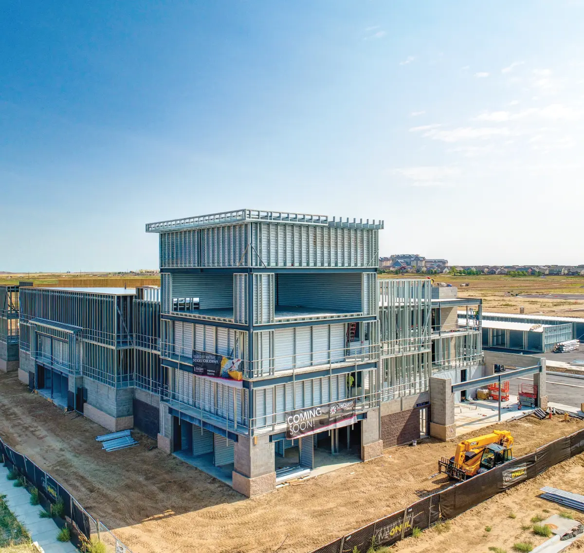 Aerial view of a multi-story self-storage facility under construction, featuring exposed steel framing and a "Coming Soon!" banner.