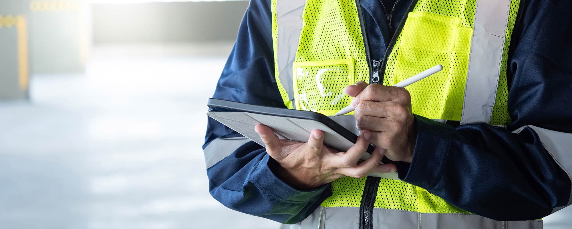 Close-up of a worker wearing a high-visibility safety vest using a stylus to write on a digital tablet.