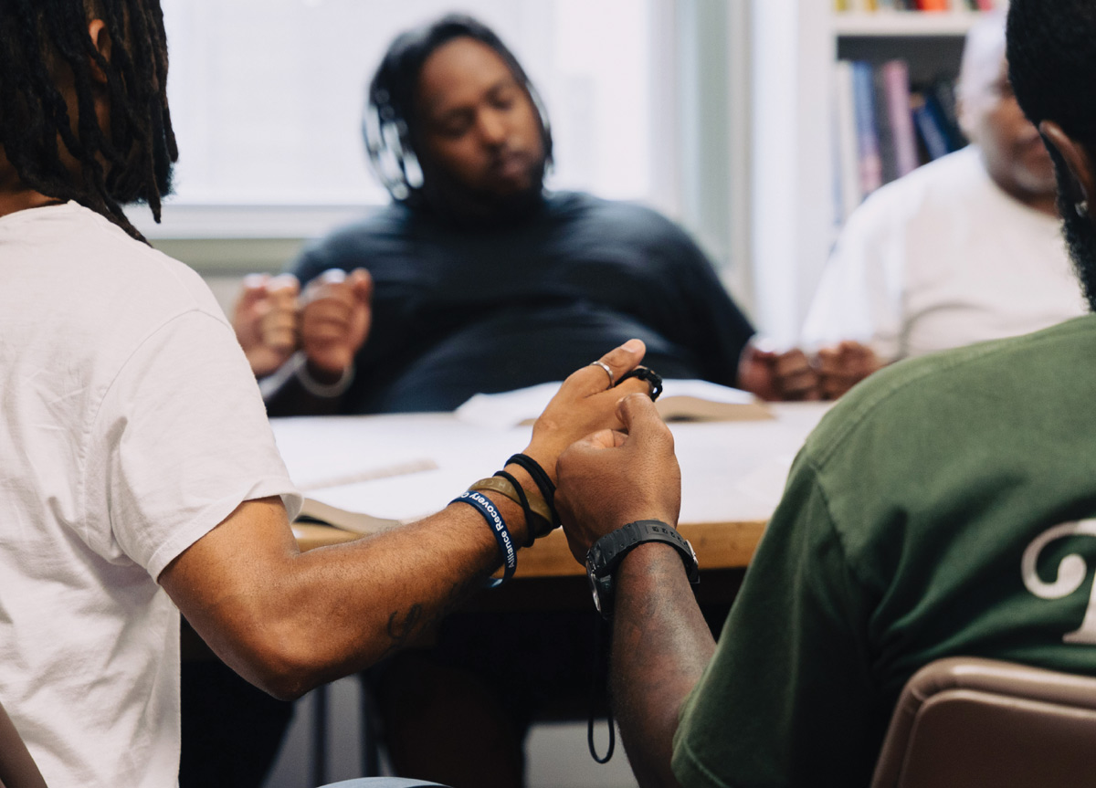 A group of people sitting around a table hold hands in a circle.