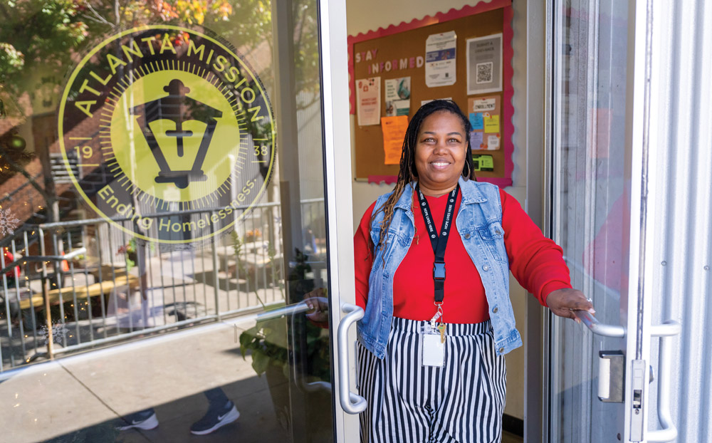 A smiling woman wearing a denim vest opens a door to the Atlanta Mission.