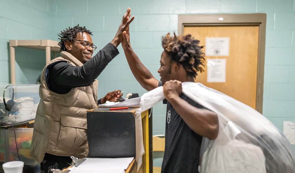 Two men smiling and sharing a high five in an indoor facility.