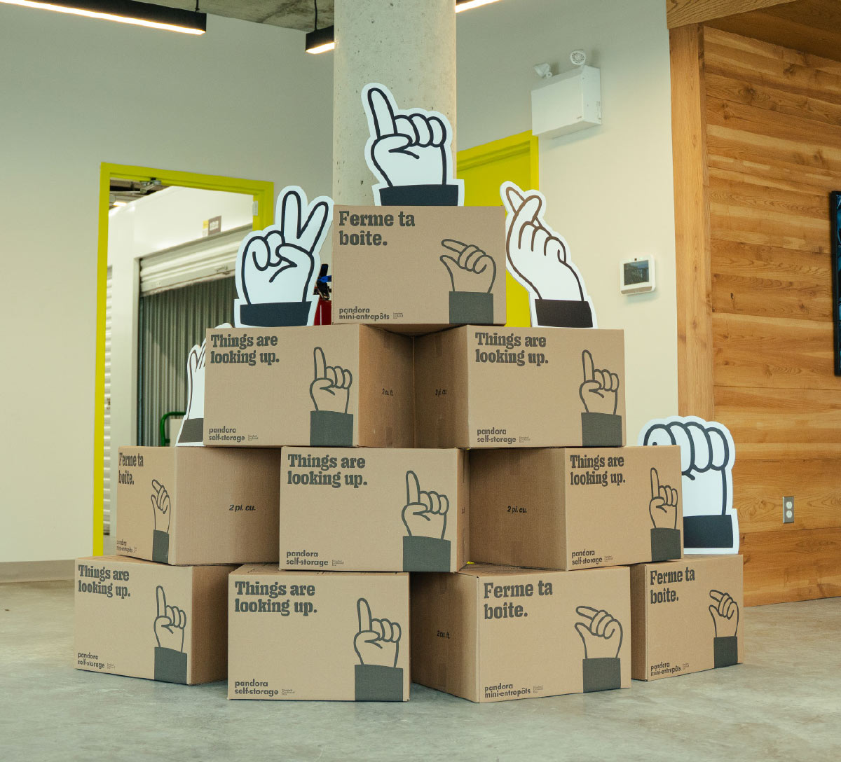Stacked cardboard boxes printed with slogans and hand-gesture cutouts inside a Pandora Mini-Entrepôts facility lobby.