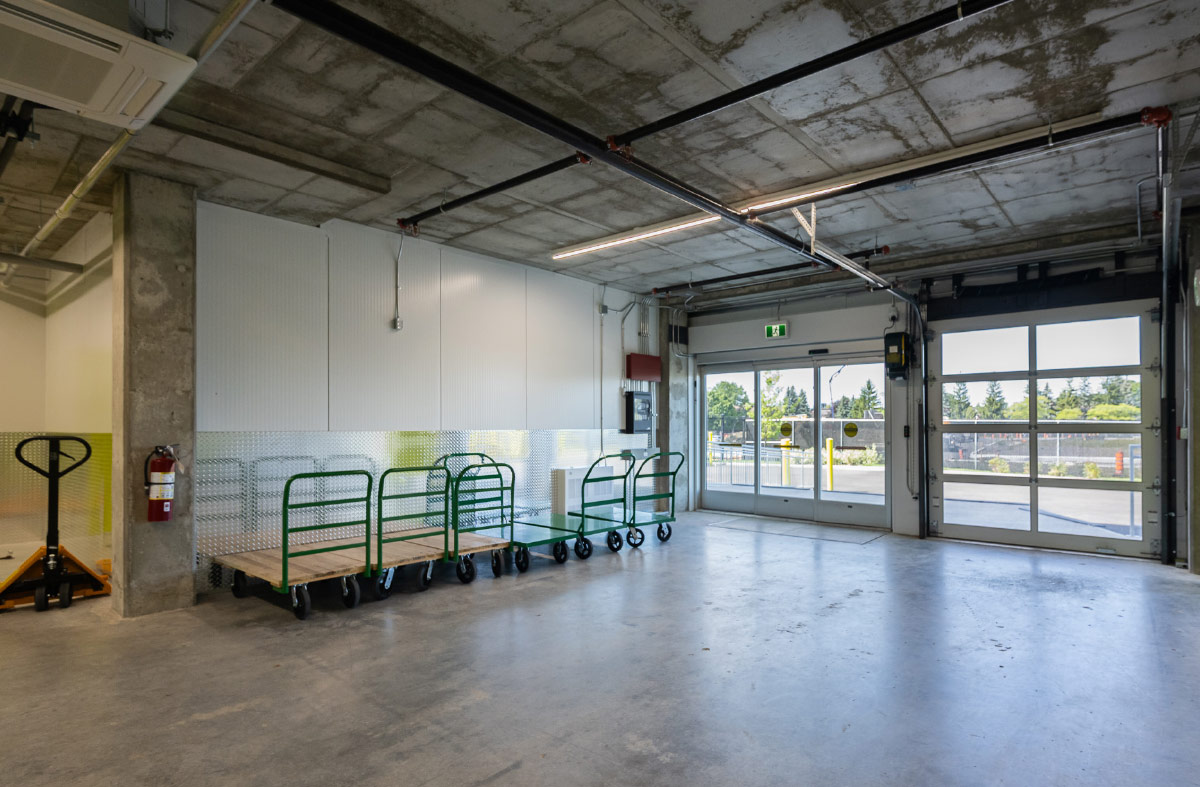 Indoor loading bay with green platform carts lined up near glass exit and overhead garage doors.