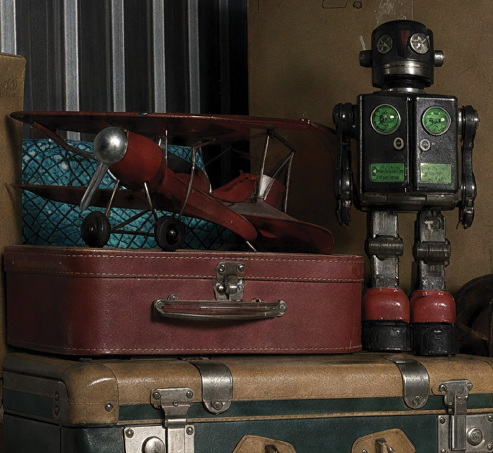 Vintage red toy airplane and a retro tin robot sitting on top of stacked antique suitcases.