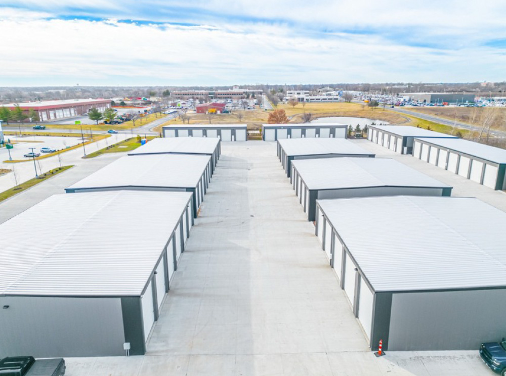 Elevated view looking down wide driveways between several rows of single-story self-storage buildings.