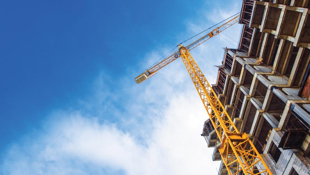 A Construction Crane Working On A Multi-Story Building Frame Against A Blue Sky.