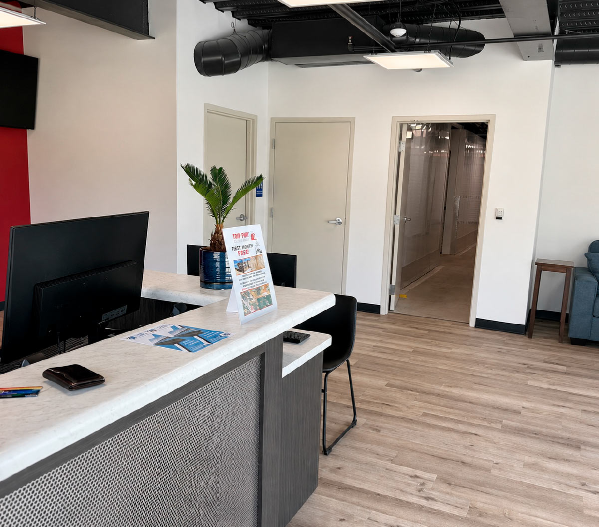 Modern self-storage reception desk area with a computer monitor, promotional flyer, and wood-look flooring.