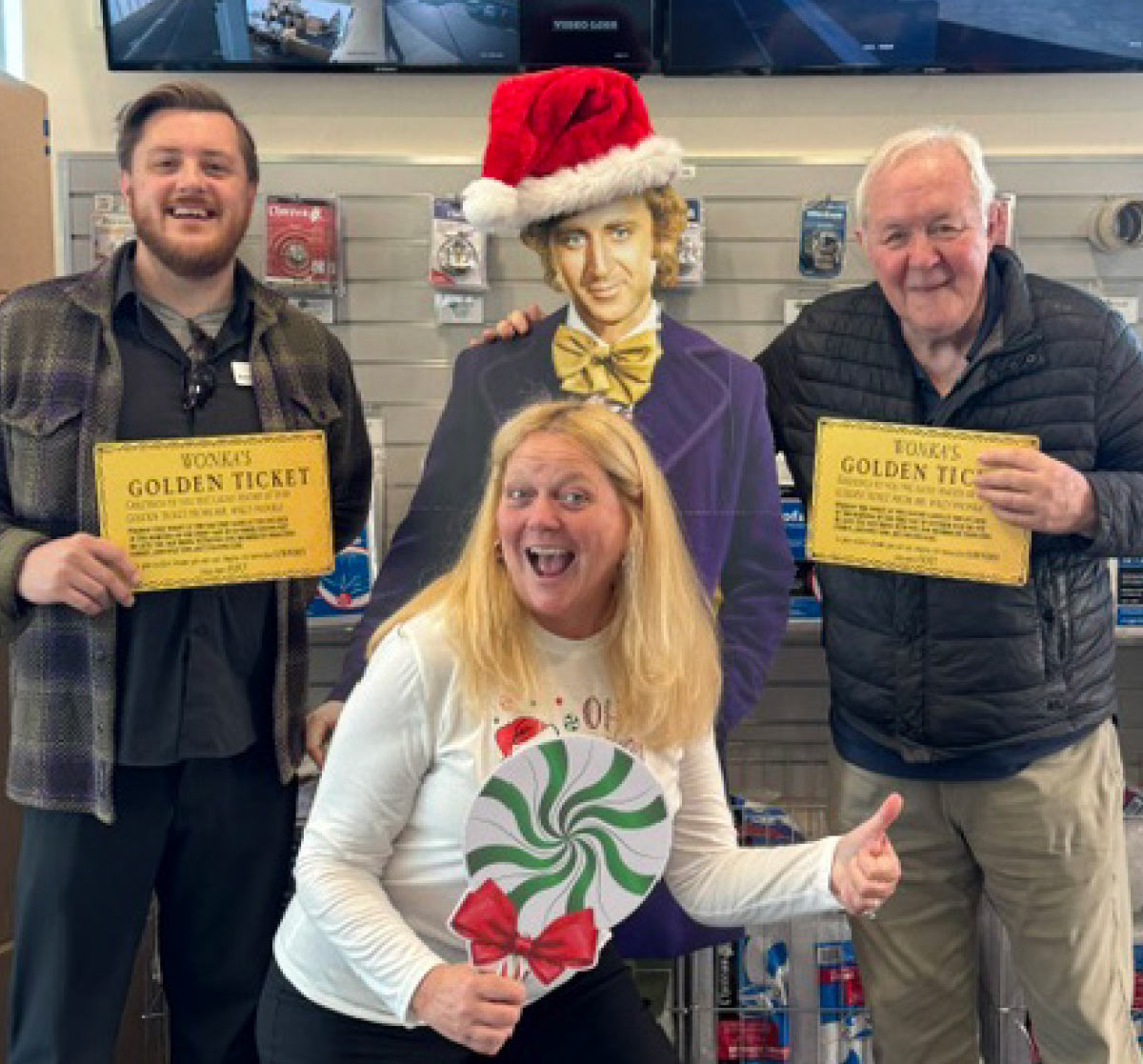 Three people posing merrily with Willy Wonka cutout and "Wonka's Golden Ticket" signs.