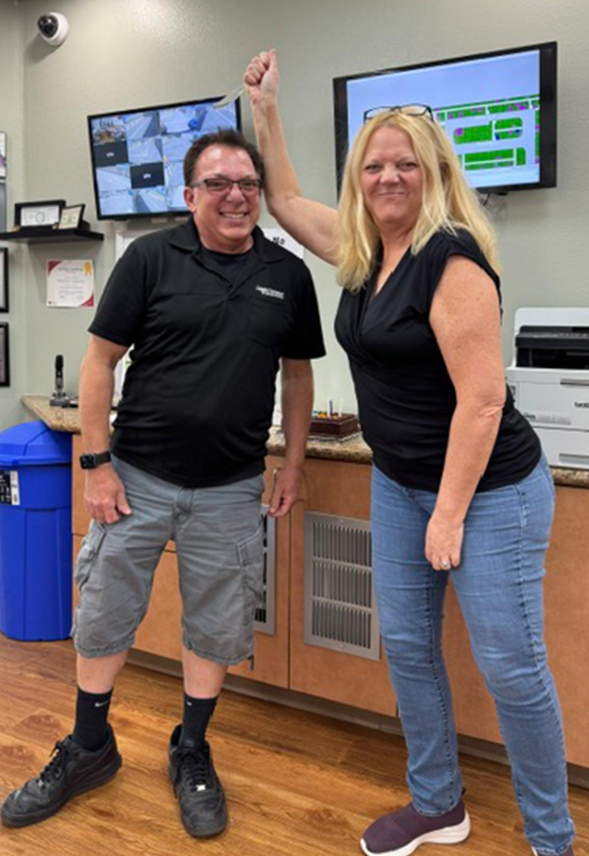 Woman jokingly holding a small knife over a man's head inside an office space.