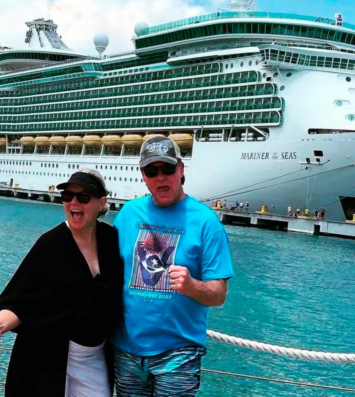 Excited couple posing on a dock in front of the Mariner of the Seas cruise ship.