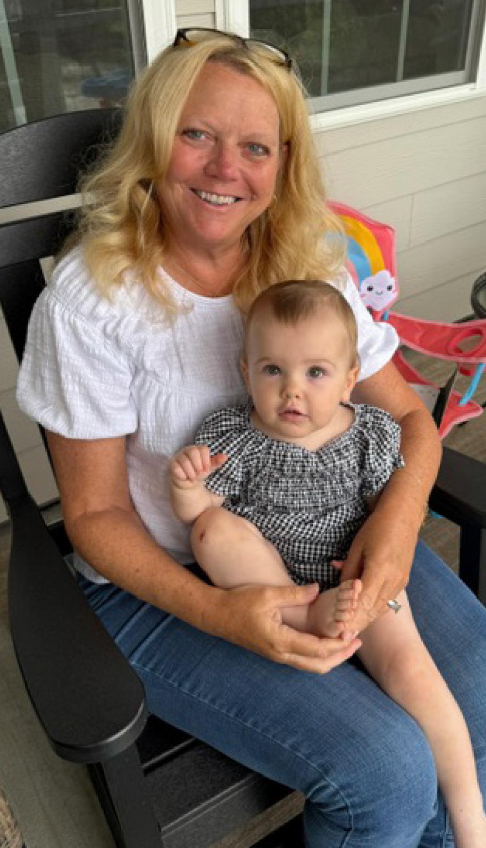 Sue Haviland sitting in a chair outdoors on a porch holding a baby on her lap.