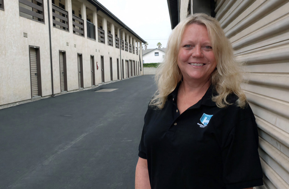 Sue Haviland in a black polo shirt standing outside a row of self-storage units.