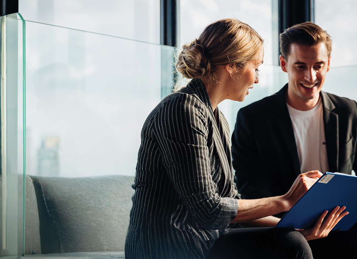 Two office professionals discussing documents held in a blue folder.