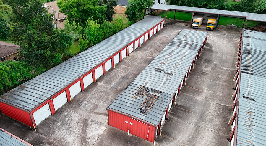 High-angle drone shot highlighting rusted and damaged panels on a self-storage roof.