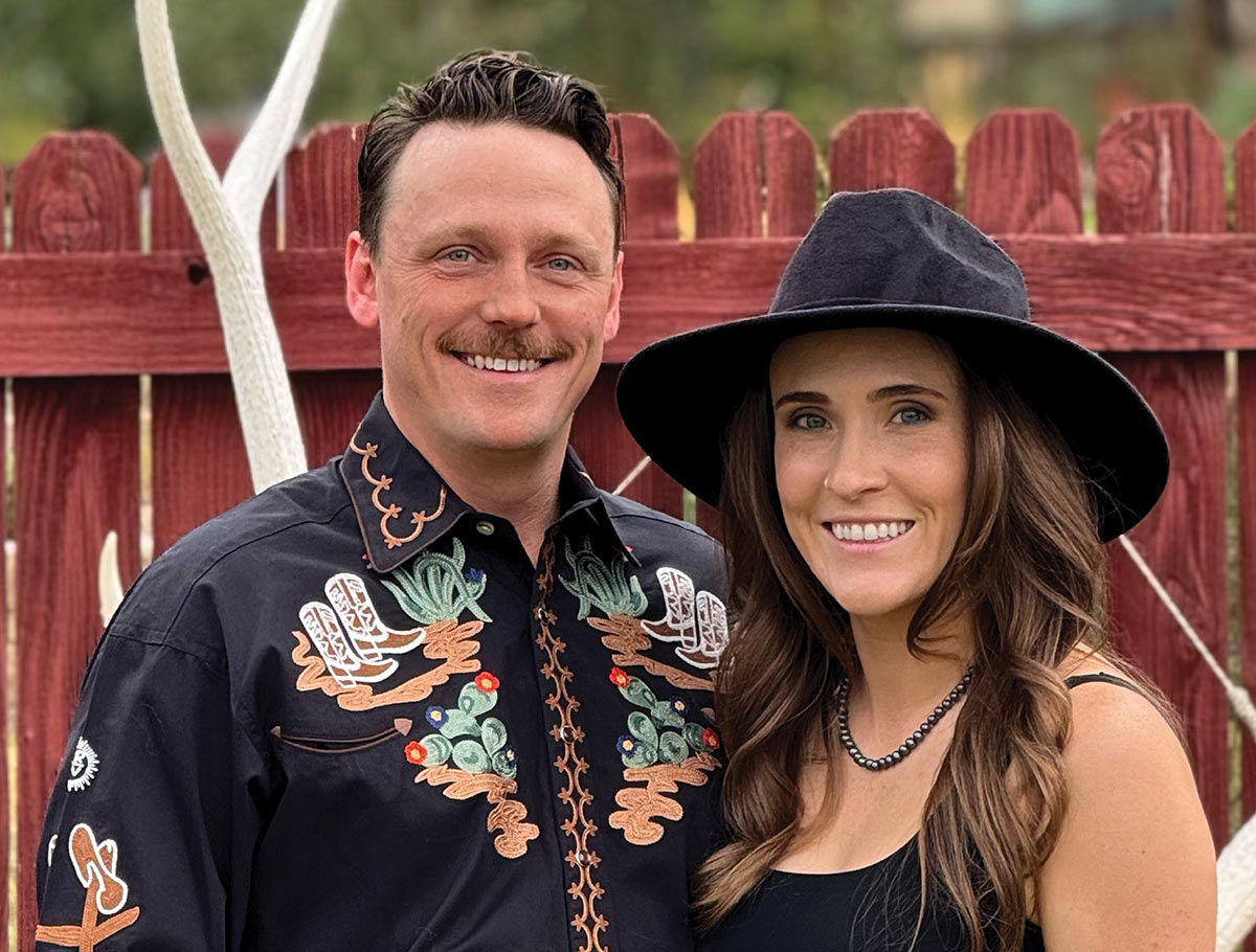 Jessie Smith and her husband Austin smiling in front of a red fence.