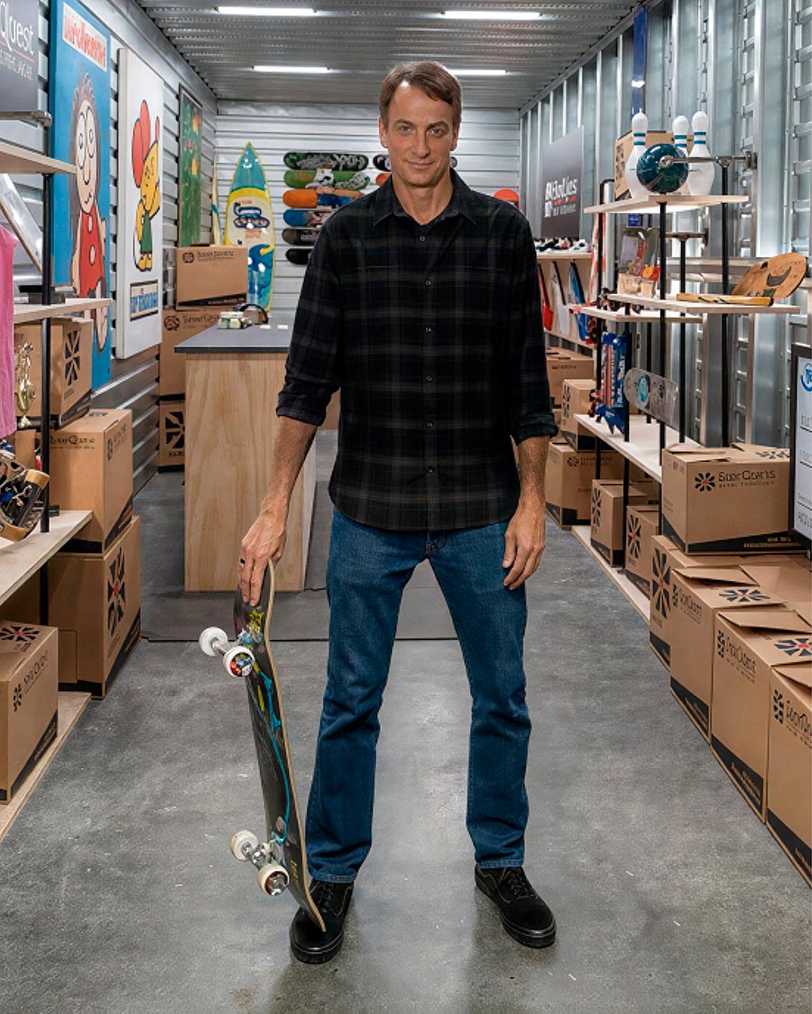 Professional skateboarder Tony Hawk standing in his organized storage unit with a skateboard.