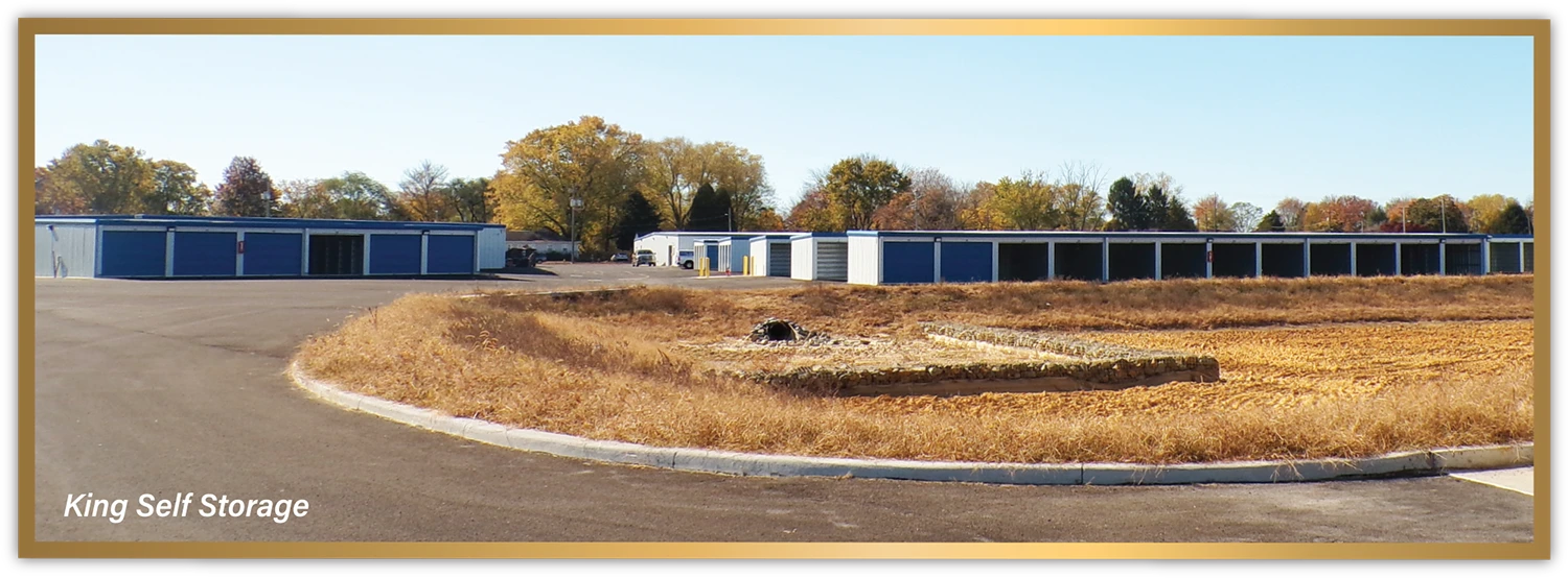 Wide outdoor view of blue single-story King Self Storage units surrounding a paved driveway and grassy field.